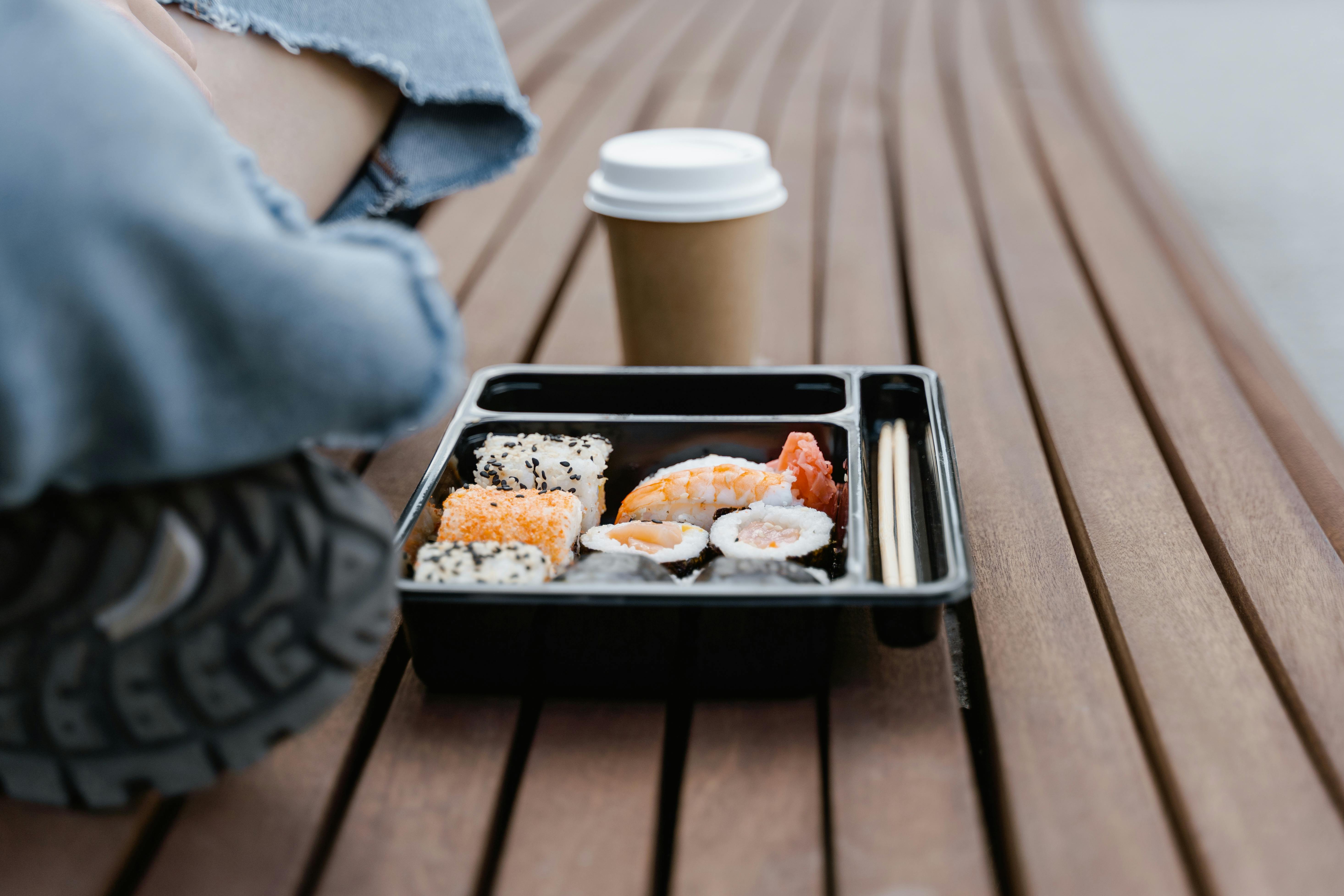 Sushi packaging made of black plastic, and a disposable paper coffee cup